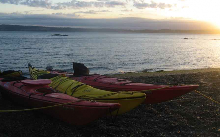 empty kayaks sit on the beach at sunset